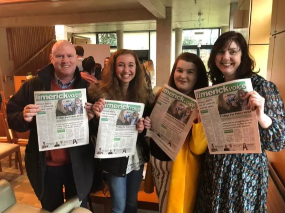 One man and three women holding copies of a newspaper smiling at the camera