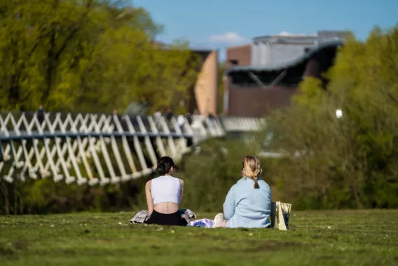 two students sitting on grass overlooking a bridge