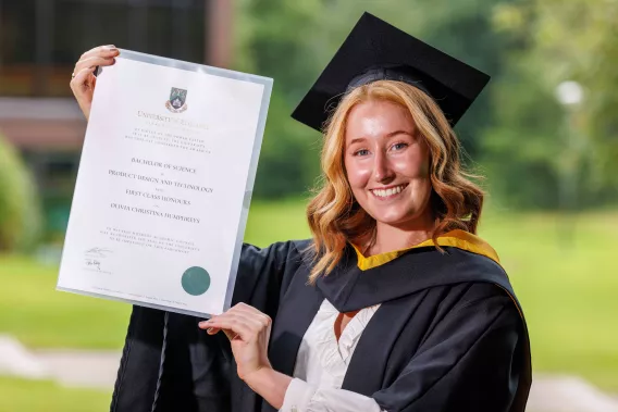 Woman in graduation robes smiling and holding a parchment