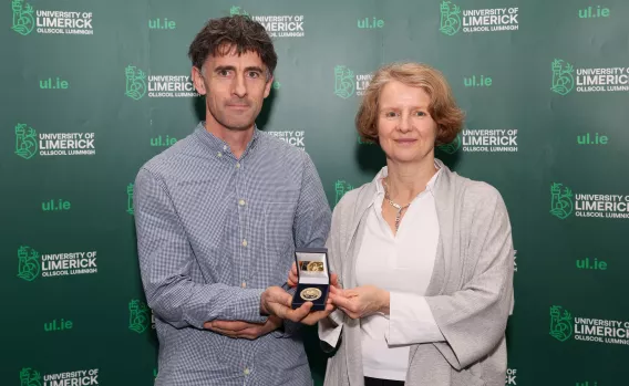 Man and woman standing in front of UL backdrop. An awards medal is being presented to the man