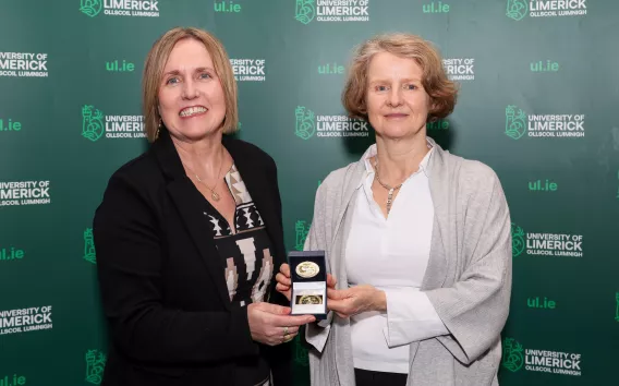 Two women standing in from of a UL branded backdrop. An awards medal is being presented