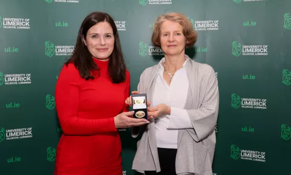 Two women standing in front of a UL branded backdrop. An awards medal is being presented to the woman on the right