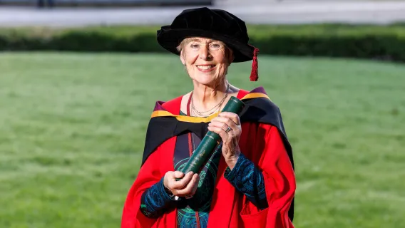 A photo of a woman in red graduation robes and black cap, holding a screen scroll in both hands