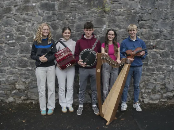 Five Irish traditional musicians standing against a wall