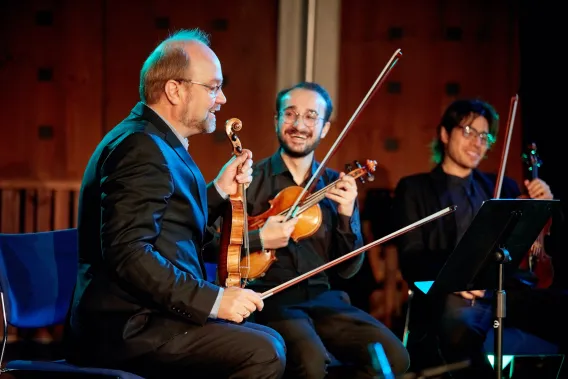 Three violinists sitting down speaking and smiling at one another