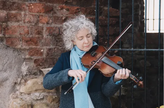 Bríd Harper plays the fiddle in front a brick wall