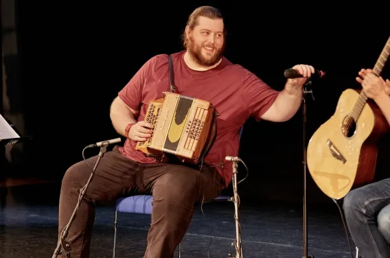 man smiling holding a microphone and an accordion