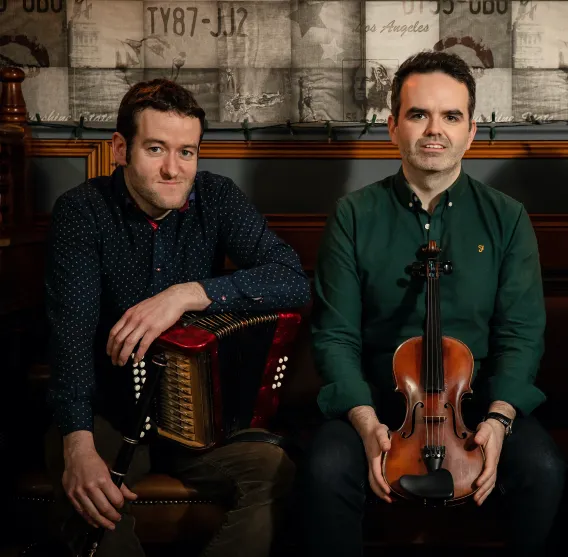 One musician holding and accordion and another musician holding a fiddle 