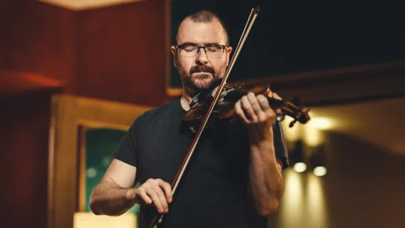 Chirs Stout wears a t shirt playing the fiddle