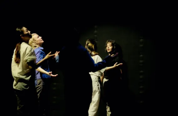 Group of dancers moving towards a dancer at the back of a dimly lit stage