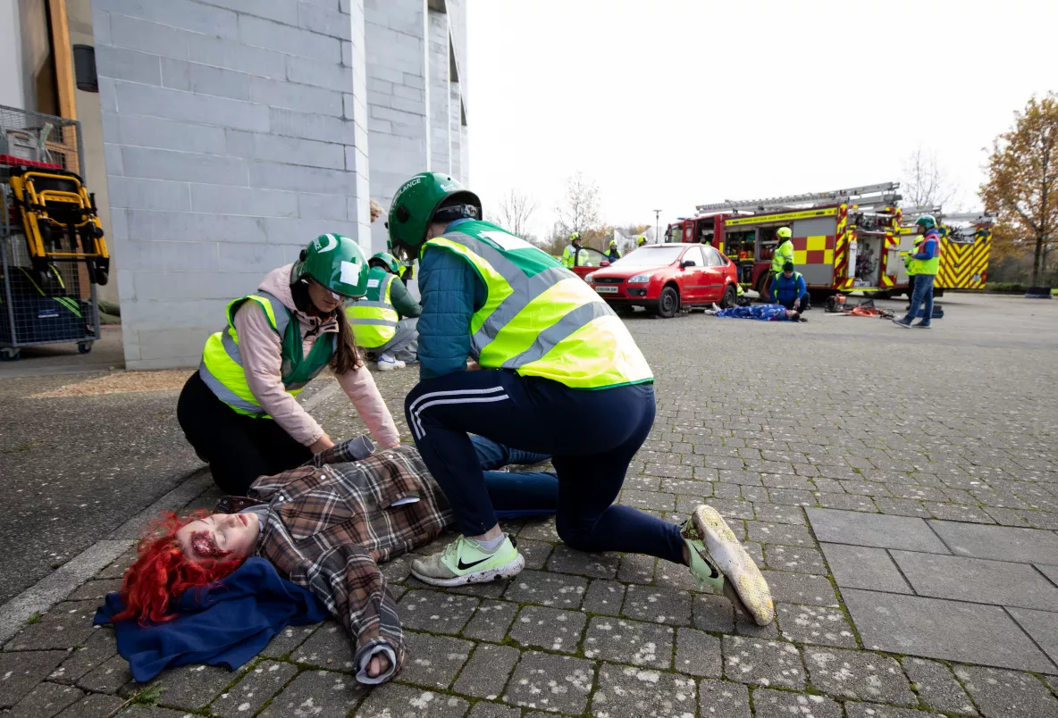 An actor victim lies on the ground while two UL student paramedics tend to her.