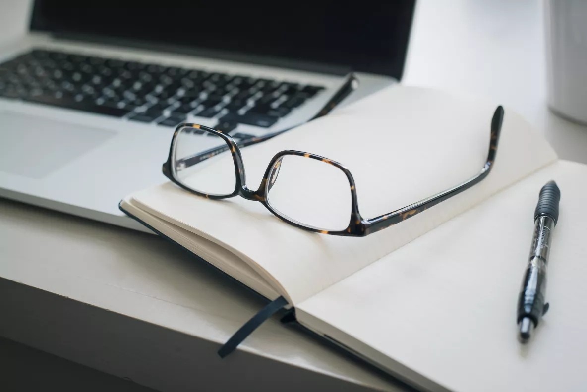 pair of glasses placed on top of an open book with a pen next to them