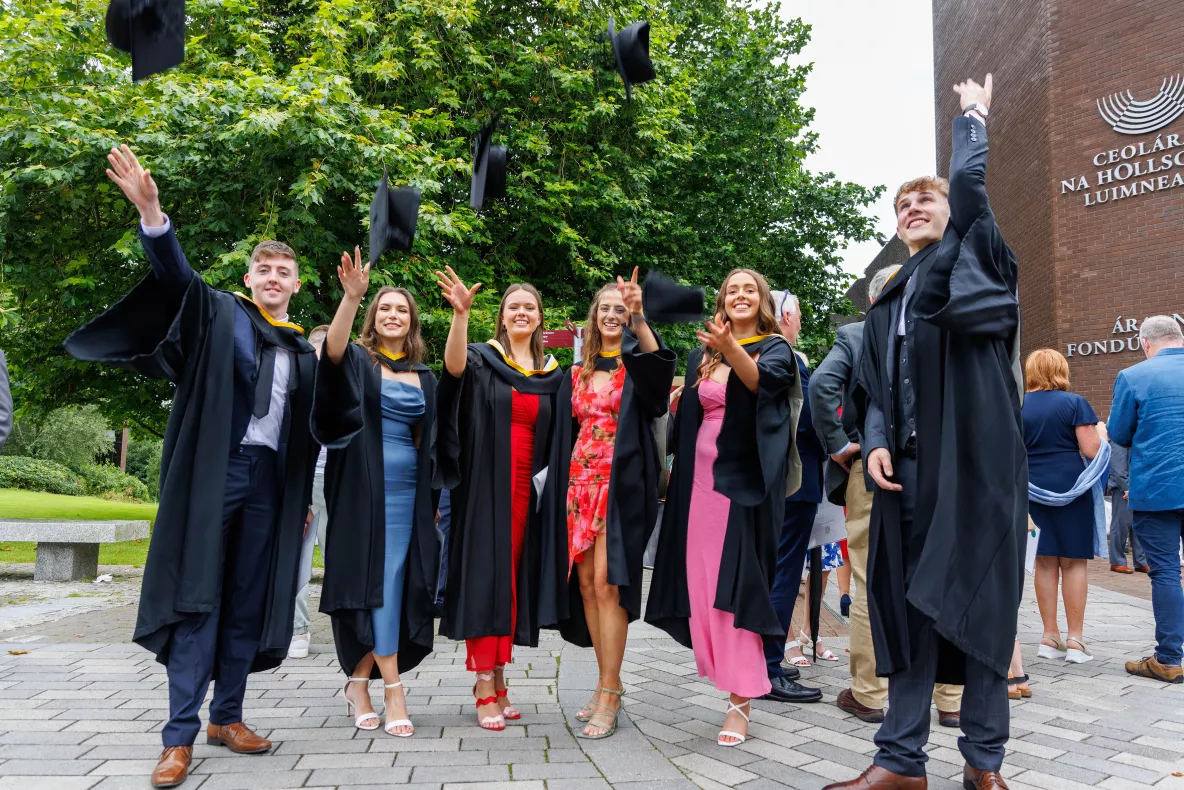 A group of students celebrate their graduation by throwing their hats in the air on the UL campus 