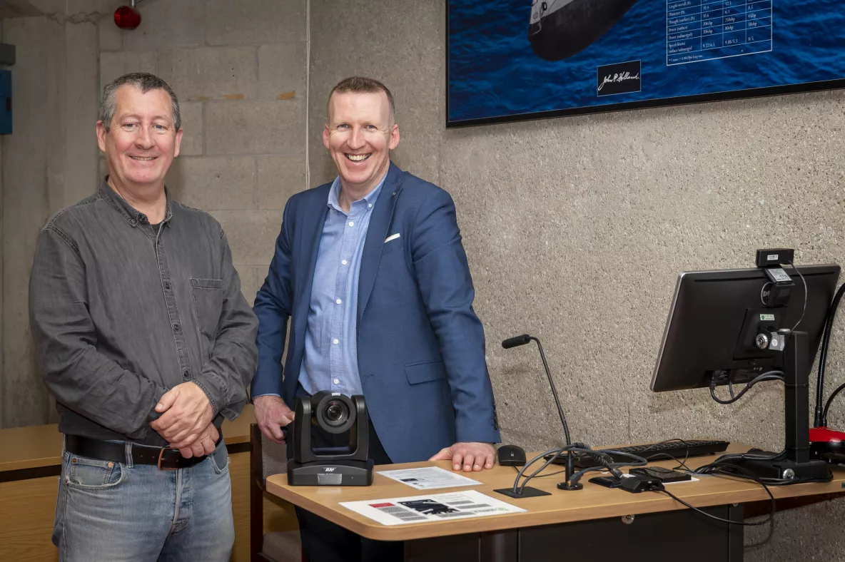 Two men standing near a desk facing the camera and smiling