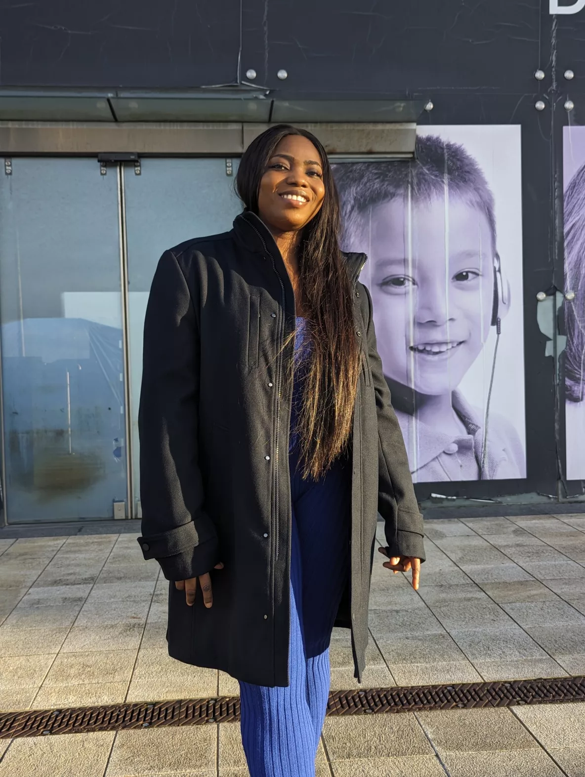 A photo of Annabel standing outside wearing a black coat and blue pants.