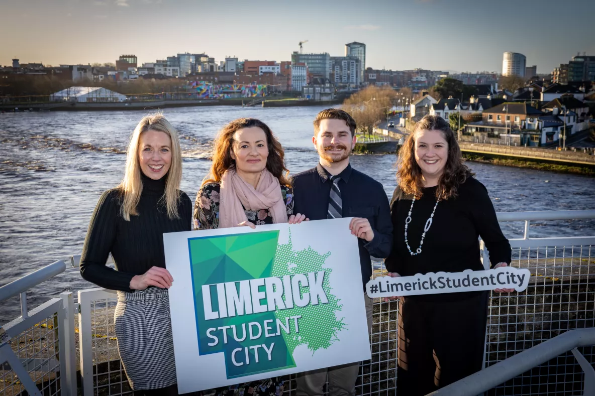 A picture of four people in front of the Shannon River in Limerick city, holding signs