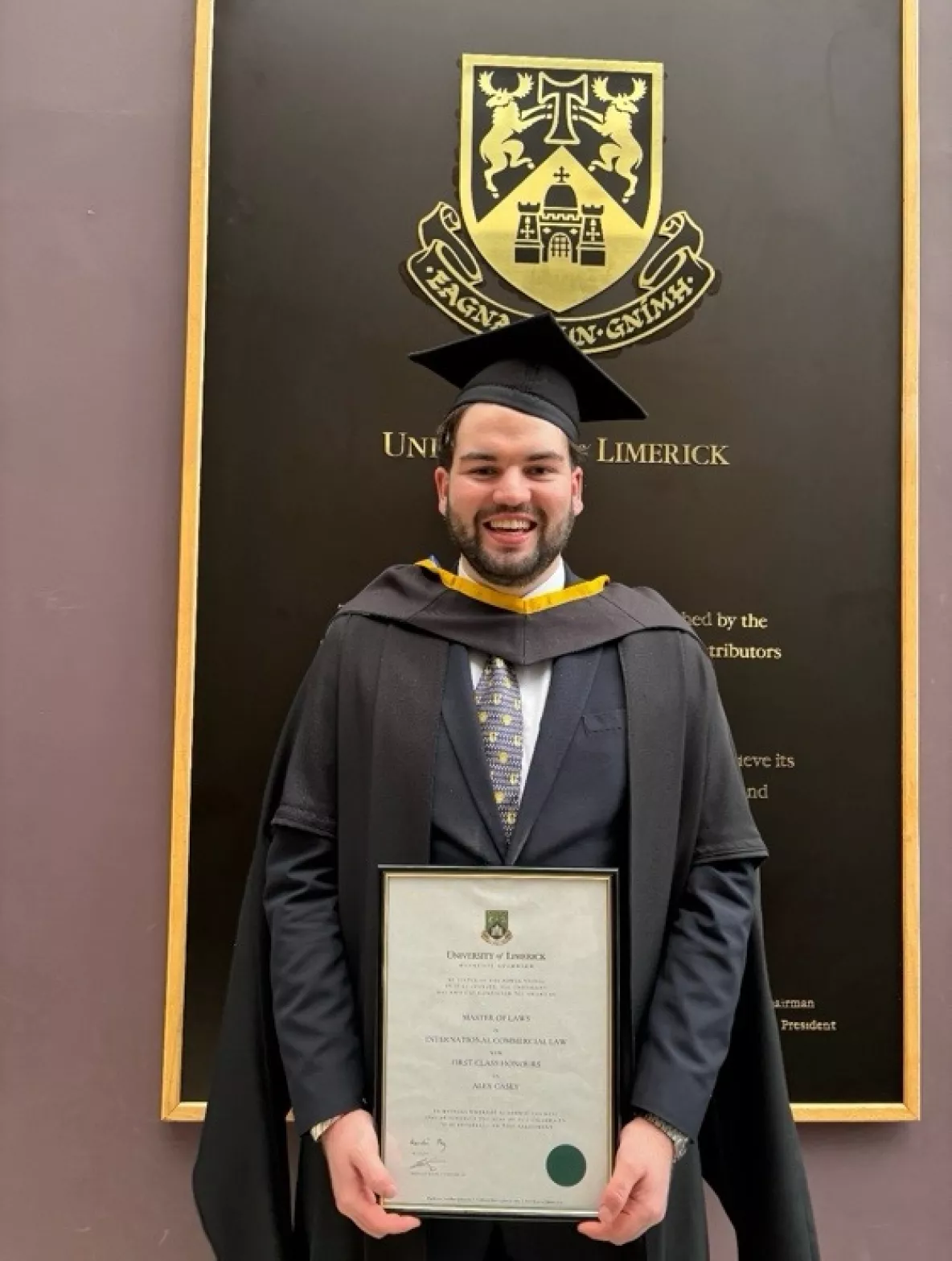 llm graduate doctor alex casey in his cap and gown holding his parchment at graduation