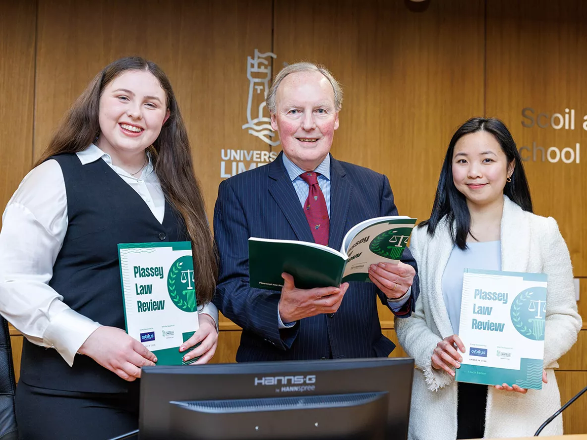 Two women and a man wearin suits smiling for a photo holding copies of the Plassey Law Review