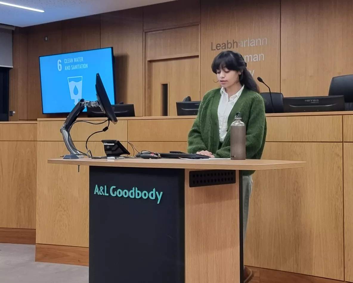 A student speaking at the podium of UL's moot courtroom. The graphic of UN SDG 6: Clean Water and Sanitation is on a digital monitor in the background.