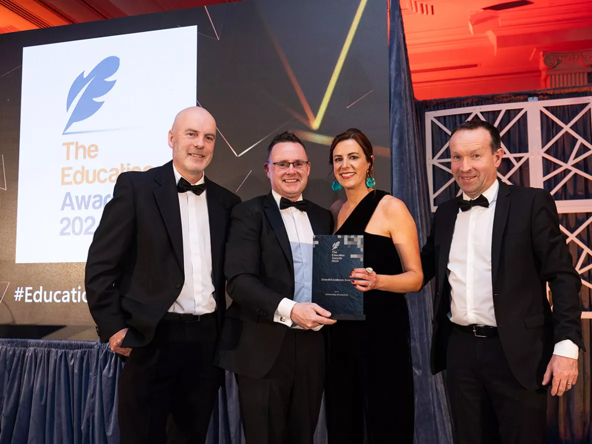 Three men and a woman in black tie clothing accepting an award on stage