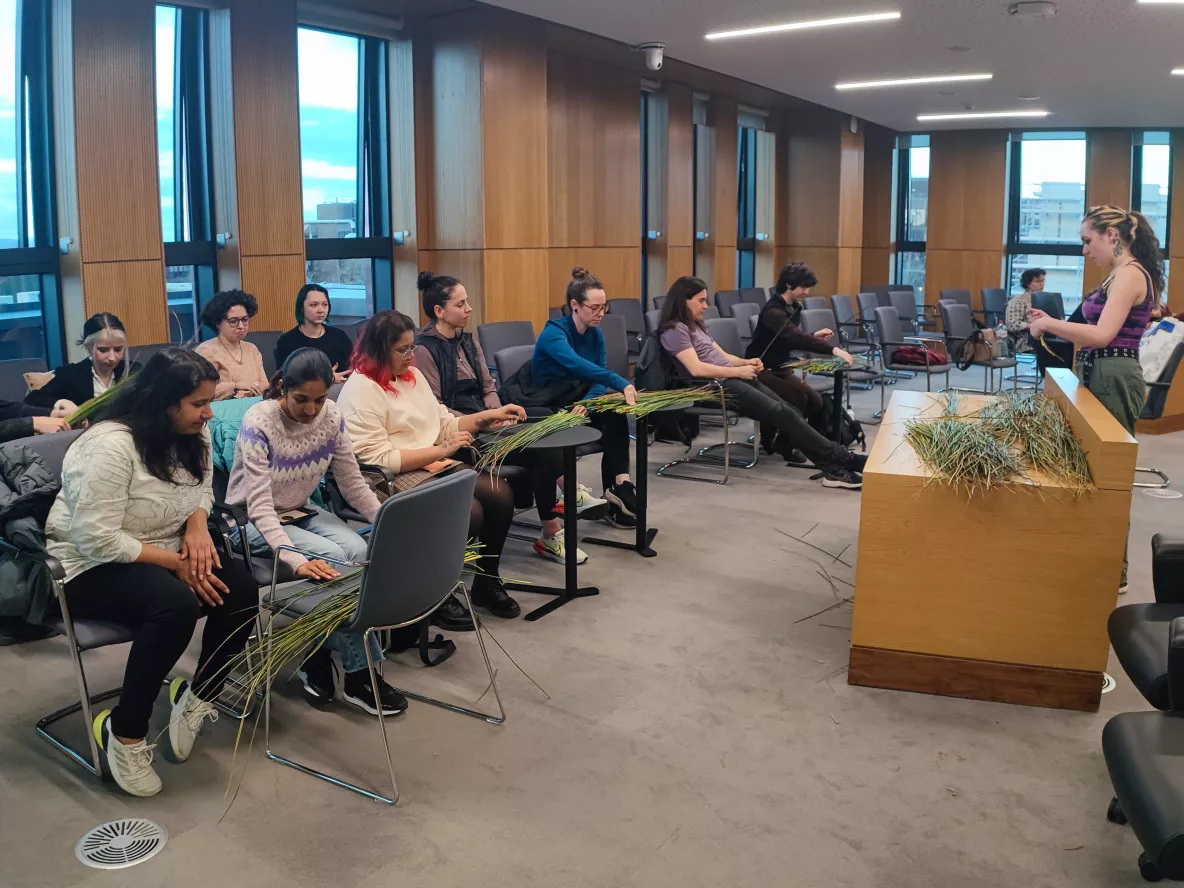 A photo of a group of students sat around a room understanding how to weave baskets with reeds