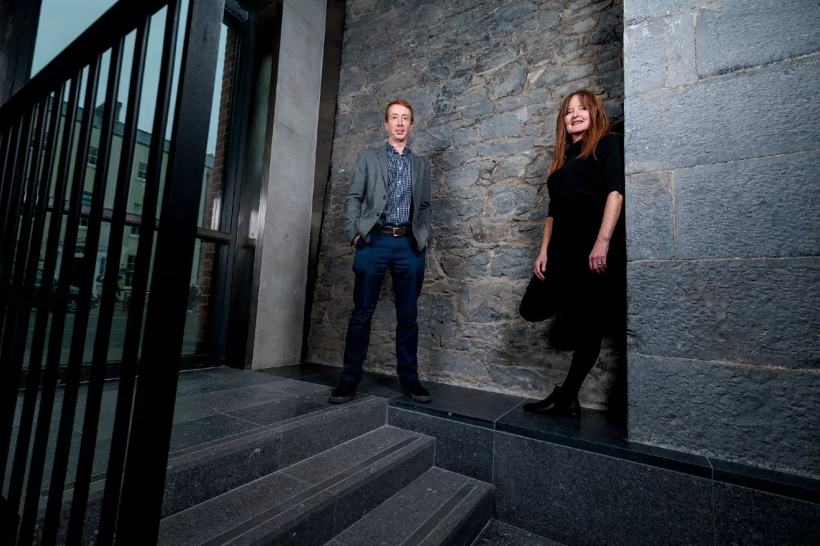 A photo of a male and female standing against a stone wall