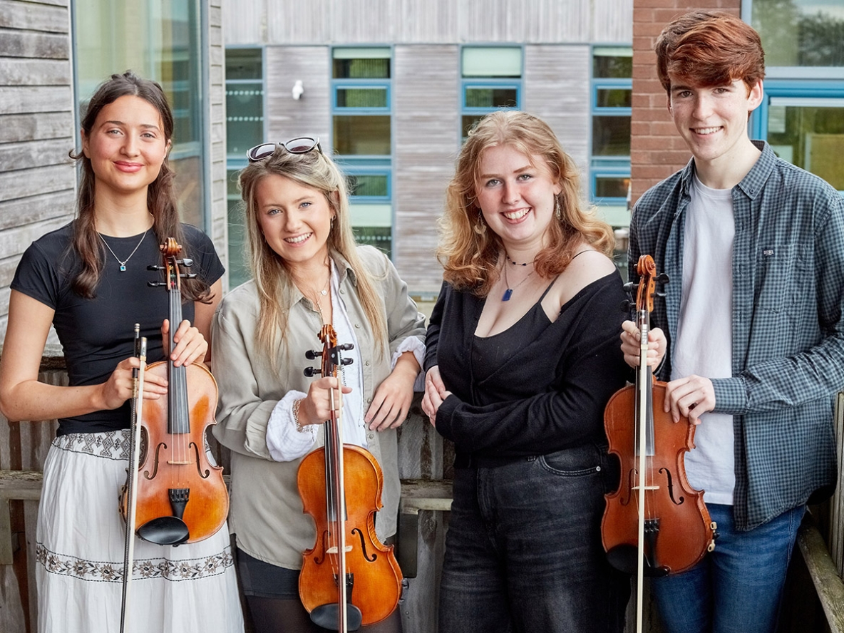 Four young adults holding violins smiling at the camera