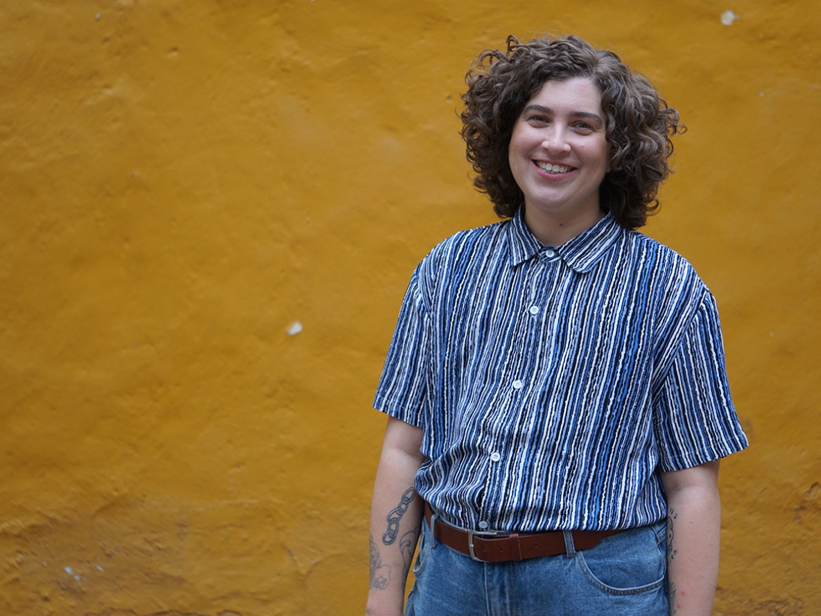 A person in a striped blue shirt and jeans standing in front of a yellow wall