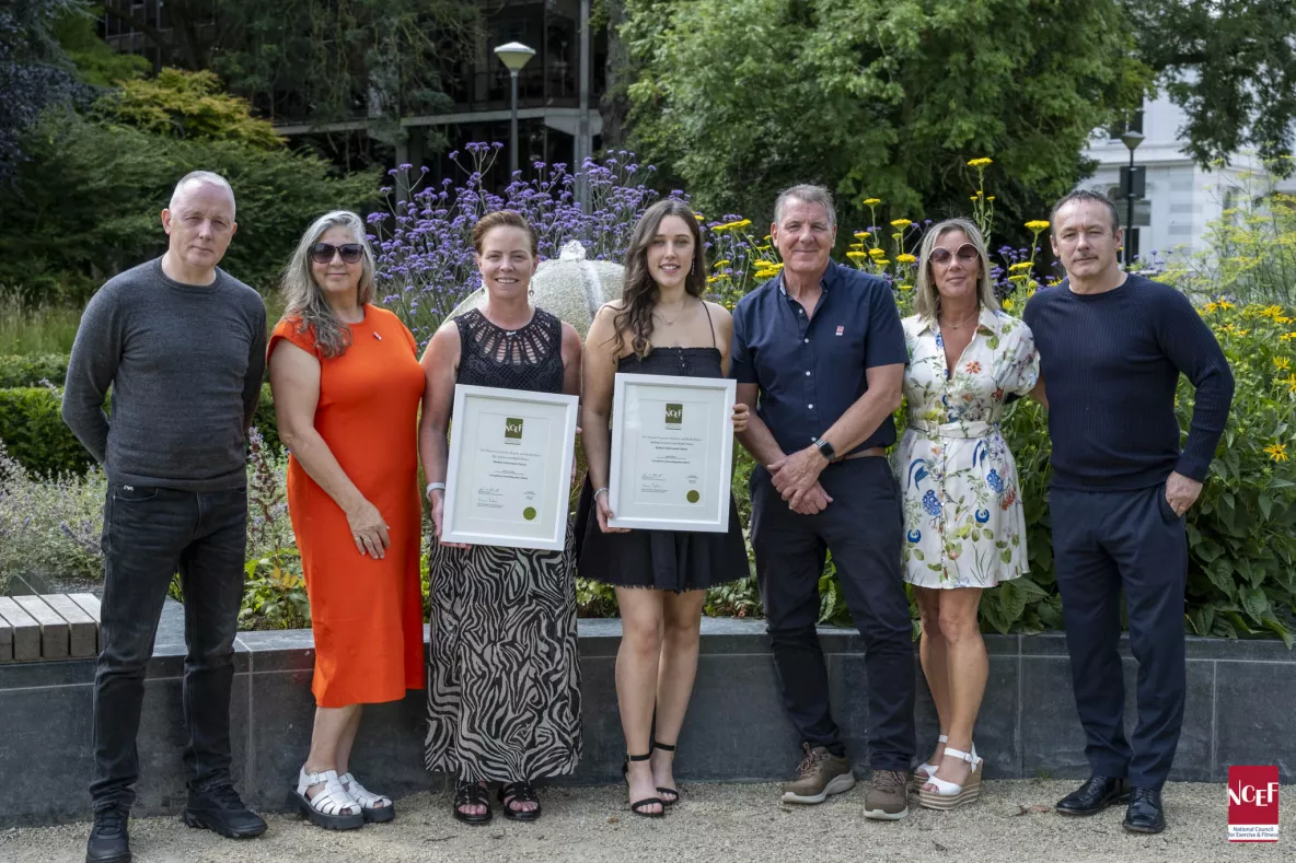 Three men and three women standing facing the camera with two women holding framed awards