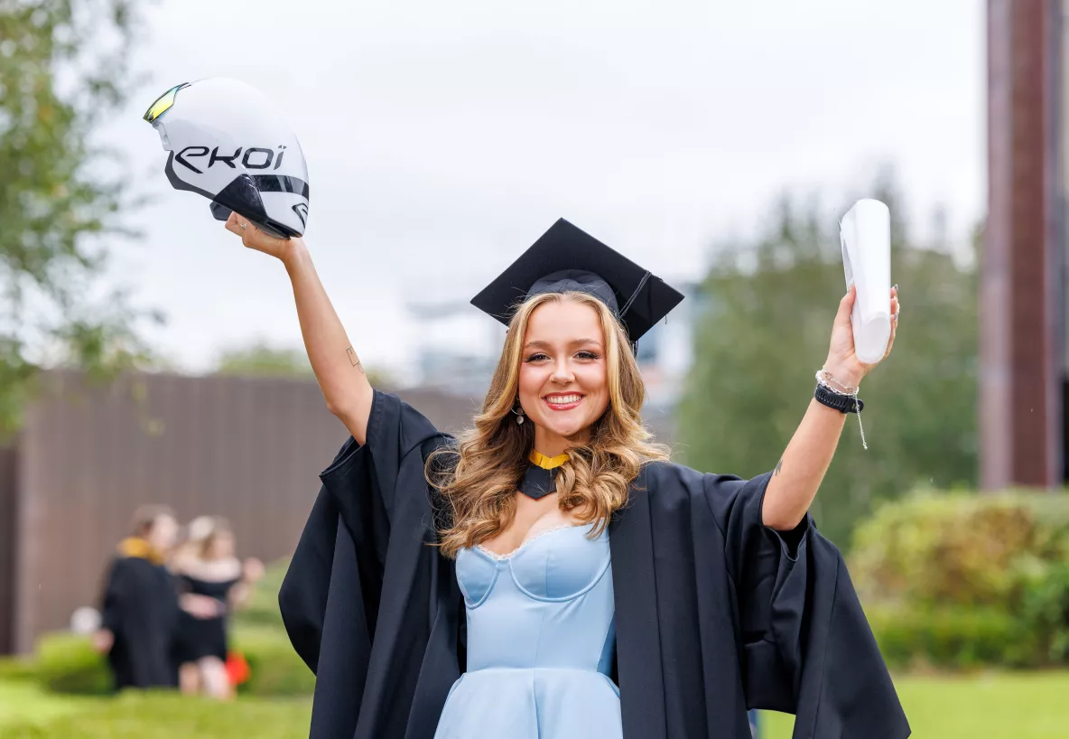 Woman graduating from university wearing a cap and gown and holding scroll and arrow helmet