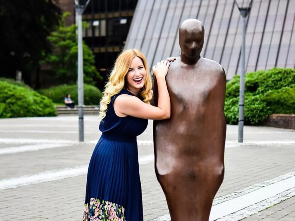 A blonde woman in a navy dress leaning on a brown statue