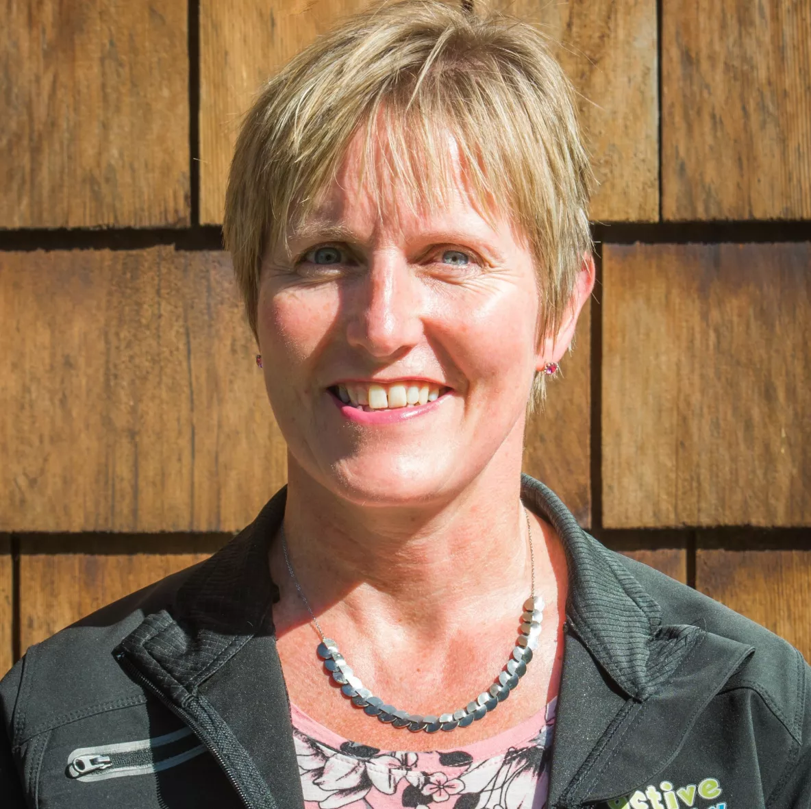 Photo of a woman with short blond hair standing against a wooden backdrop