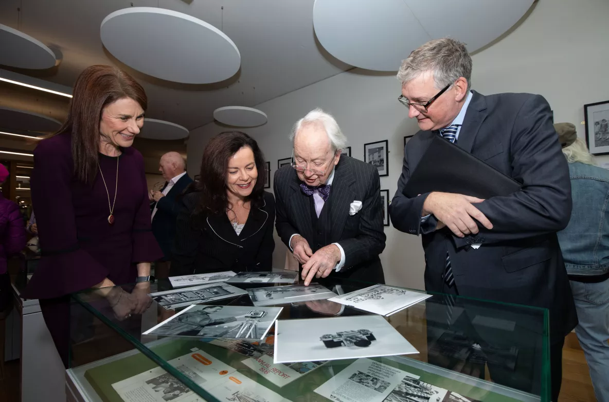 Four people looking at old photographs on top of a glass case - they are in the UL library