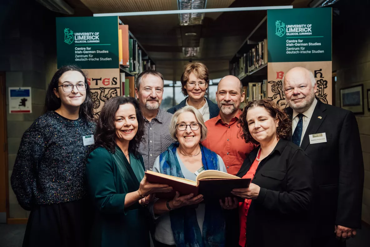 Group of people looking at large book in front of library shelves