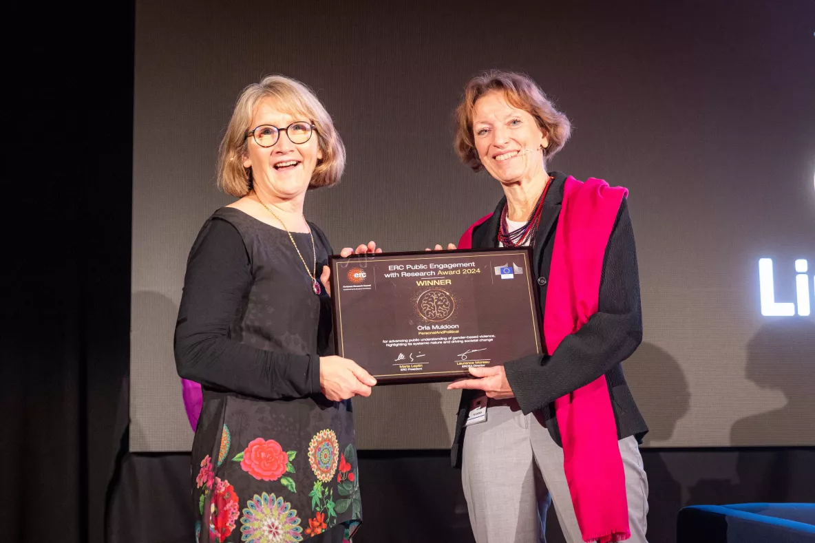 Picture of two women smiling and holding an award on a stage