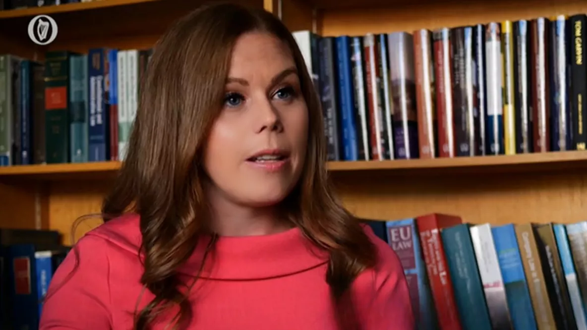 A photo of a woman speaking in front of a shelf of books