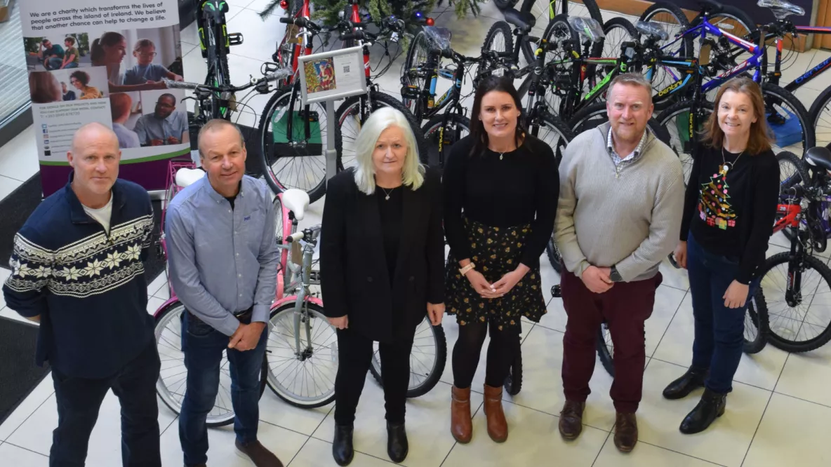 A photo of a group of people - three men and three women - standing in front of a row of bikes