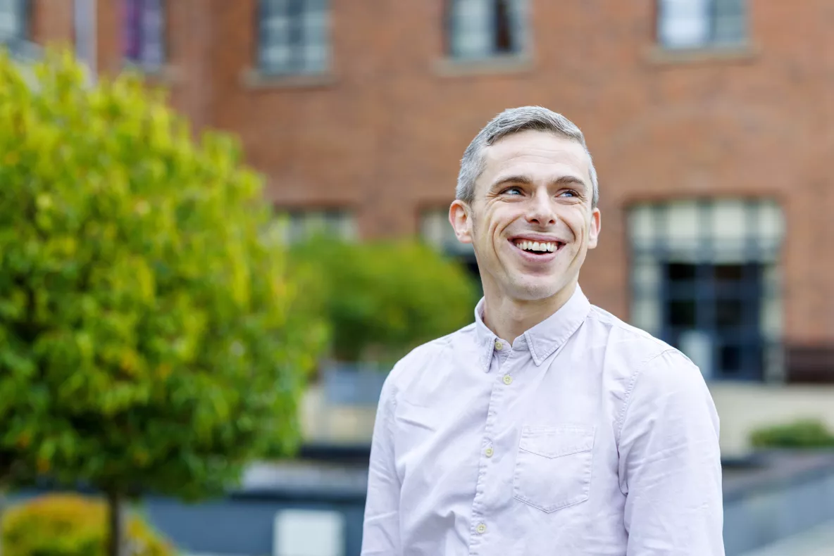 Smiling man standing outside in front of building and greenery 