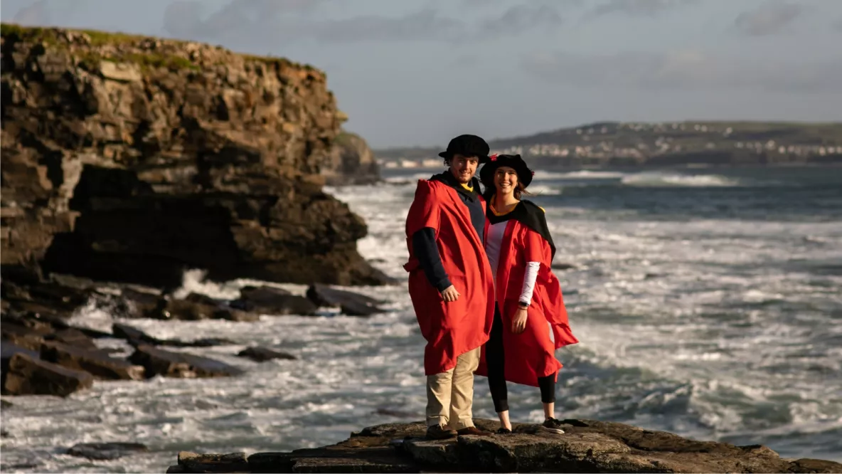 Man and woman PhD in robes posing at the beach