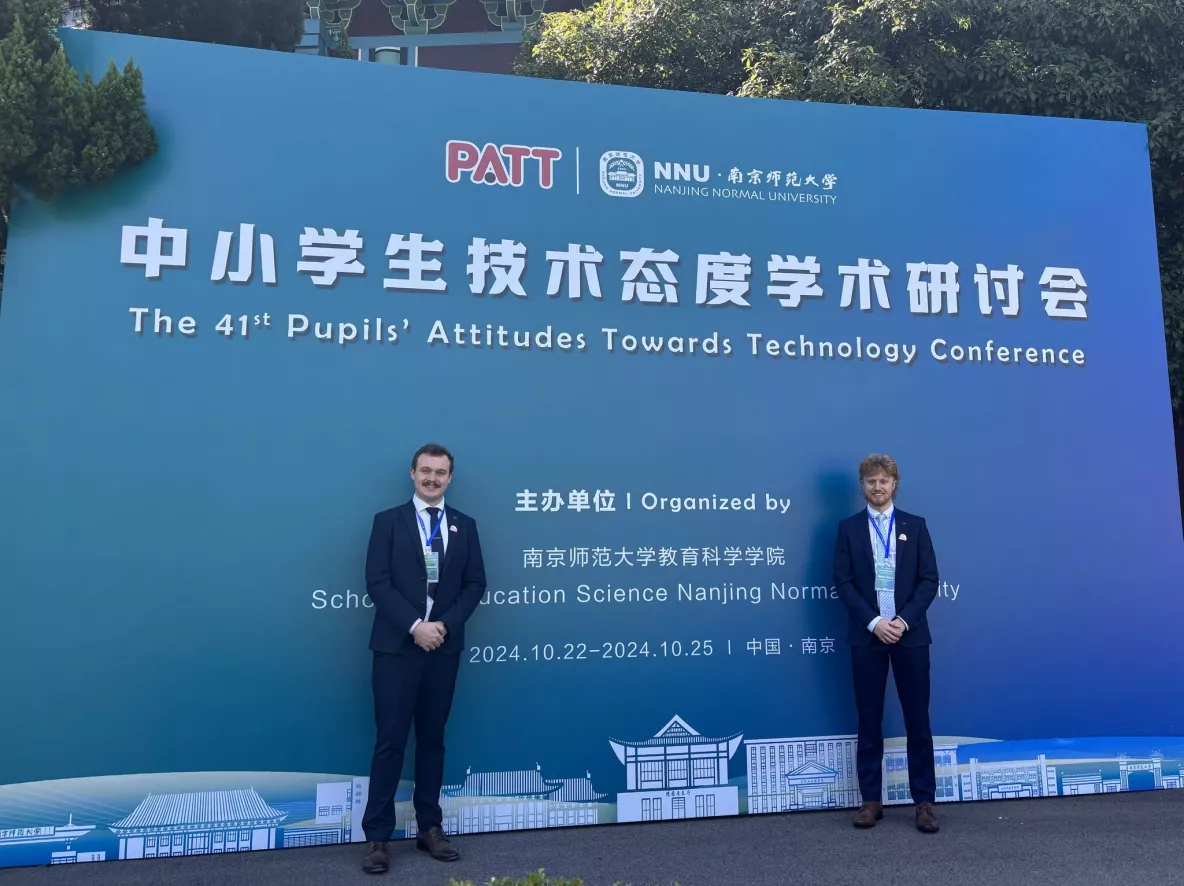 2 men in suits standing infront of a sign with Chinese writing