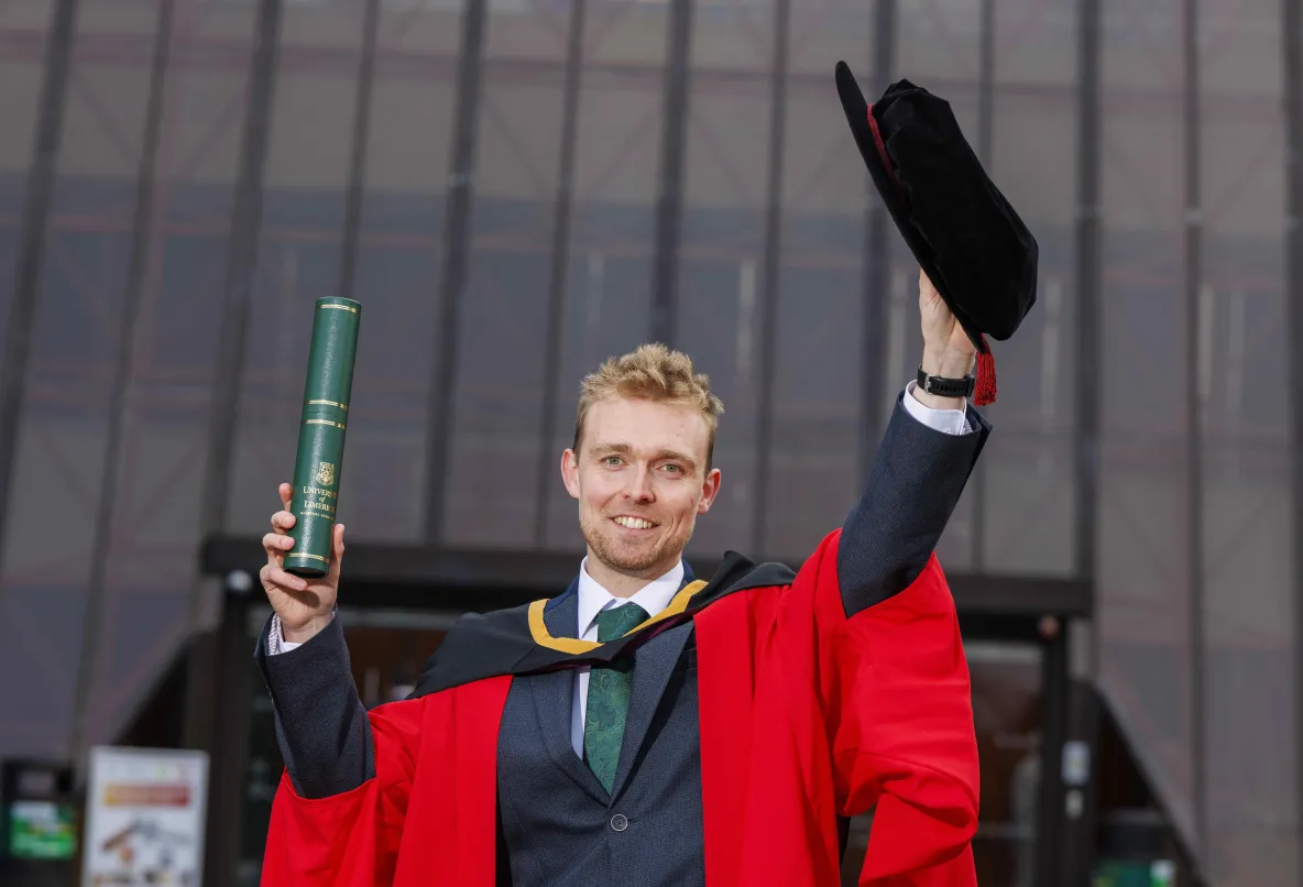 Man in red graduation robes holding a cap and scroll