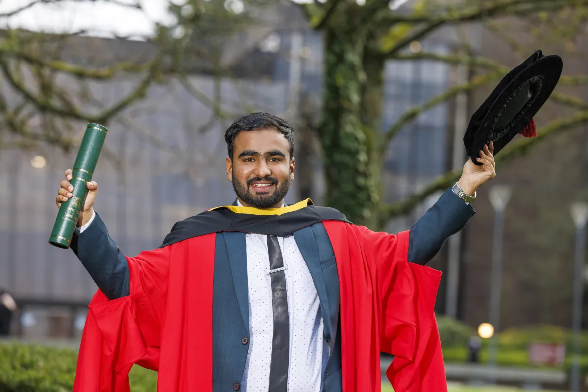 Man in PhD robes posing with hat and scroll