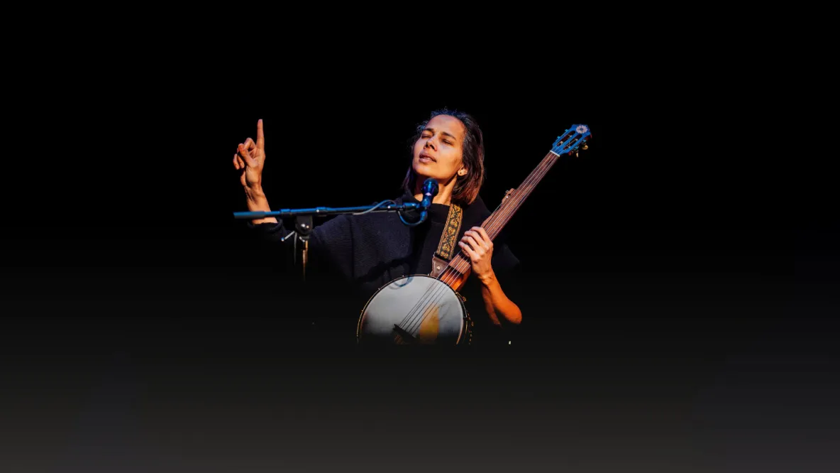 A photo of a woman playing a stringed instrument against a dark background