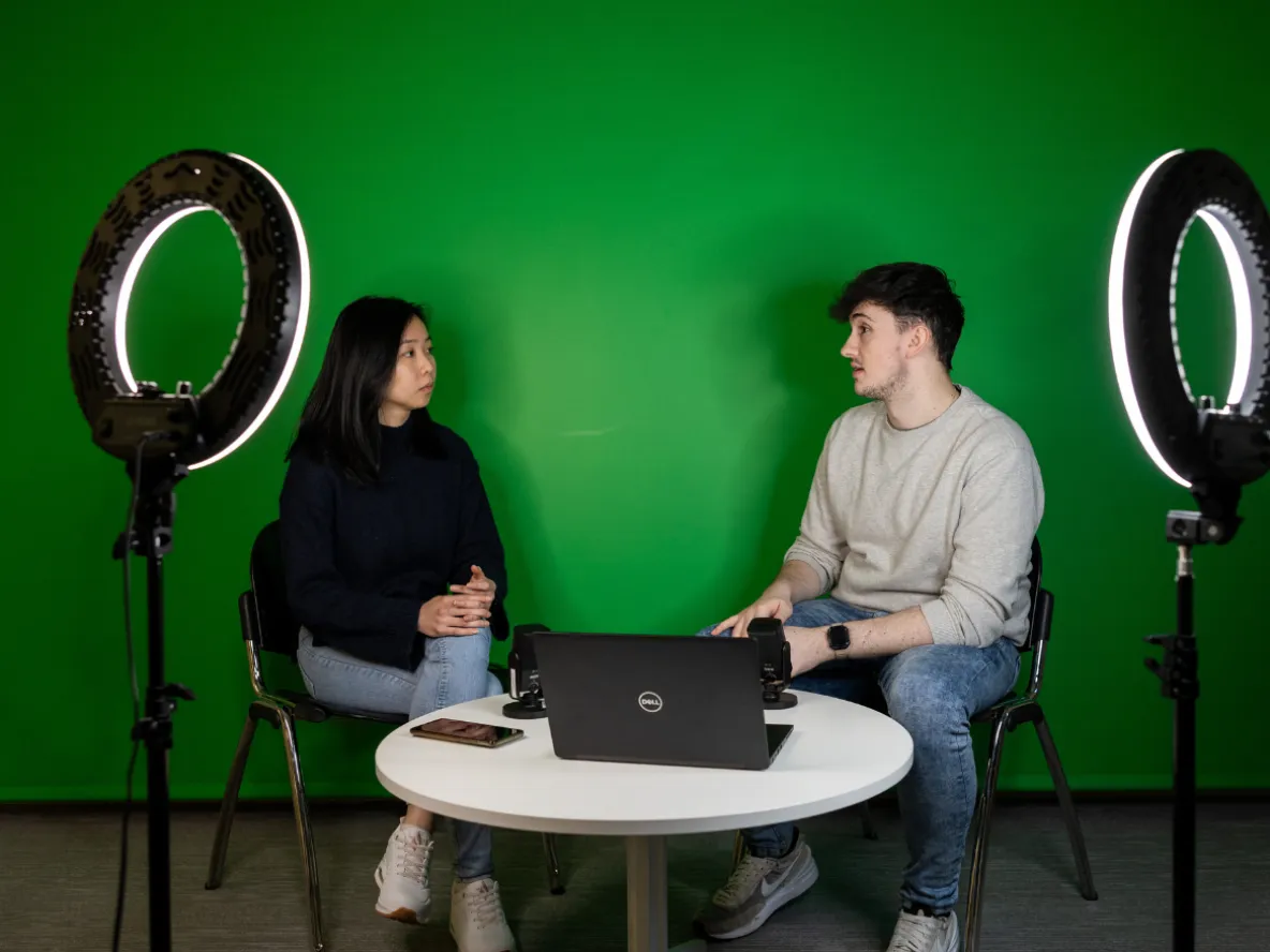 2 students in greenscreen room with laptop and ringlights