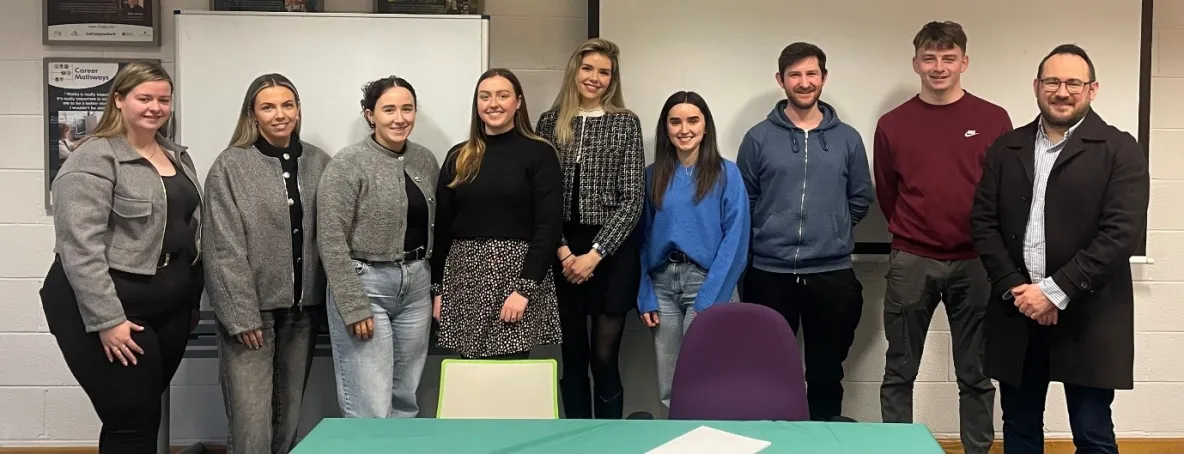 9 people standing at the front of a classroom