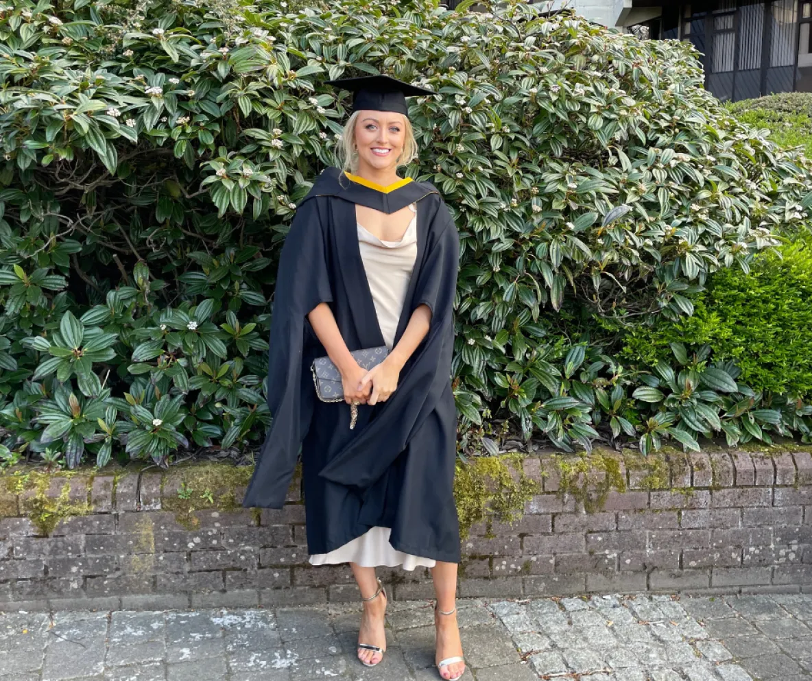 Woman in graduation robes standing in outdoor setting