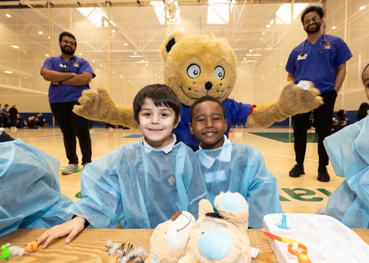 photo of two children in scrubs with giant teddy bear and two doctors behind them