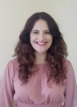 Denia headshot, long curly hair and a pink top on