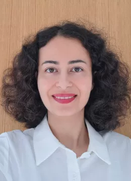 A woman with short curly hair wearing a white top and red lipstick smiling