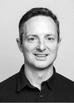 A man with dark hair, wearing a black shirt smiling